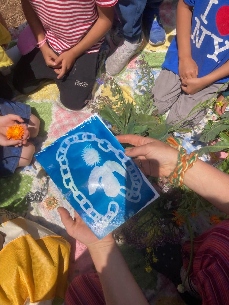 Photo of hands holding out a blue cyanotype print surrounded by children