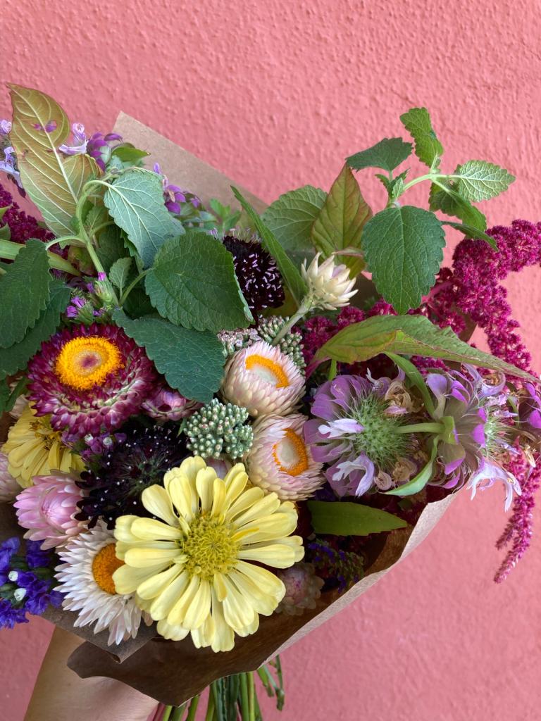 close up image of a bouquet with yellow, pink, and multicolored flowers with green foliage. set against a light red background.