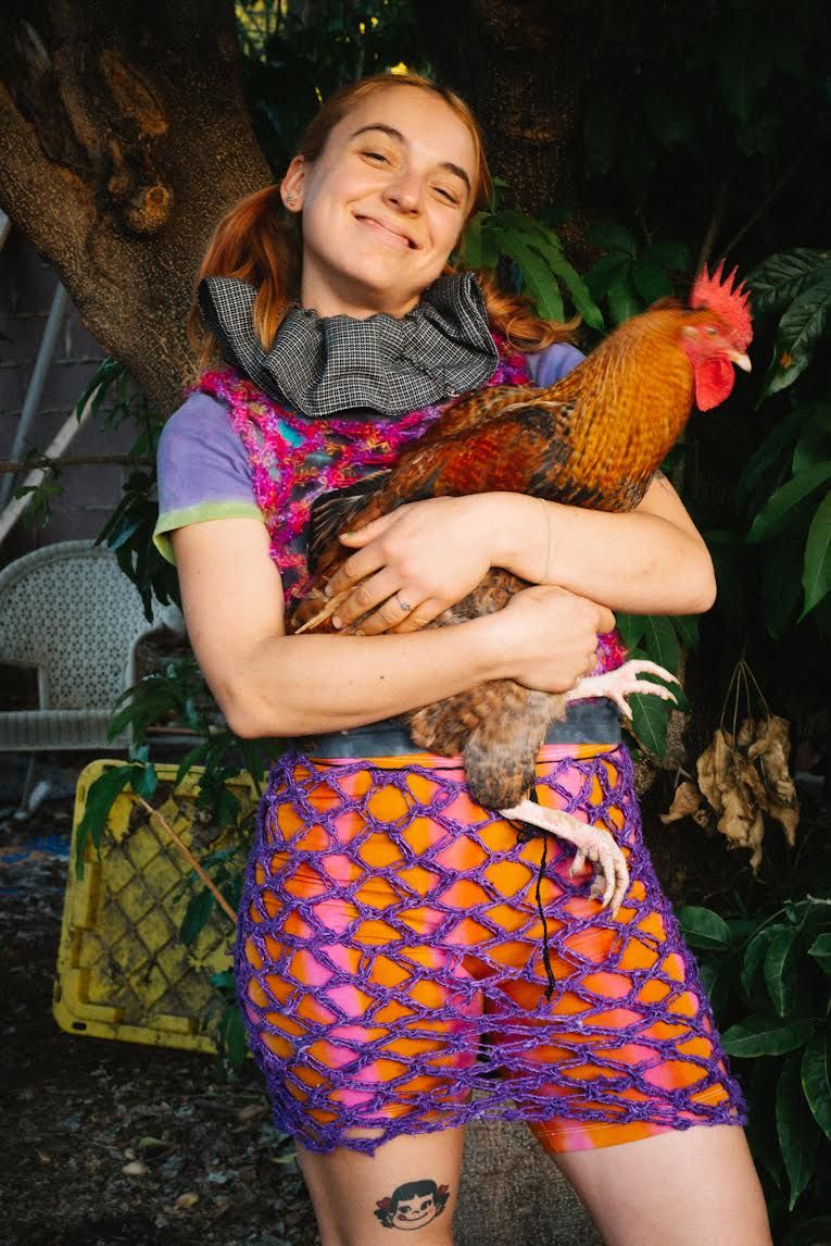 A person with light skin is smiling and holding a rooster in their arms