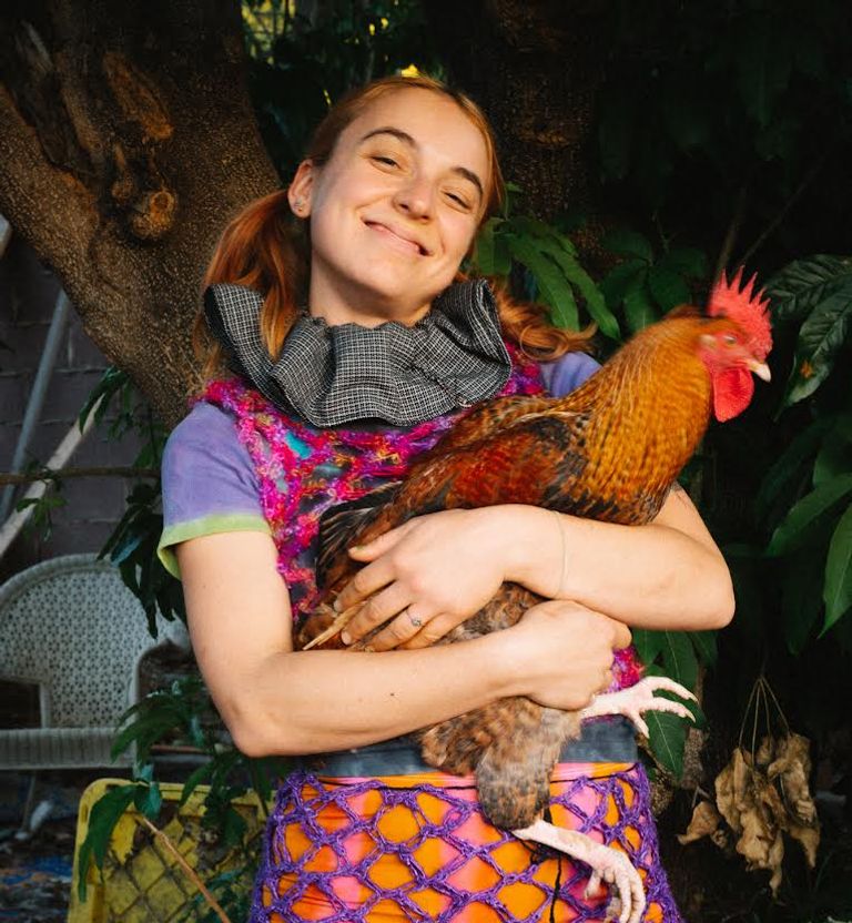 A person with light skin is smiling and holding a rooster in their arms