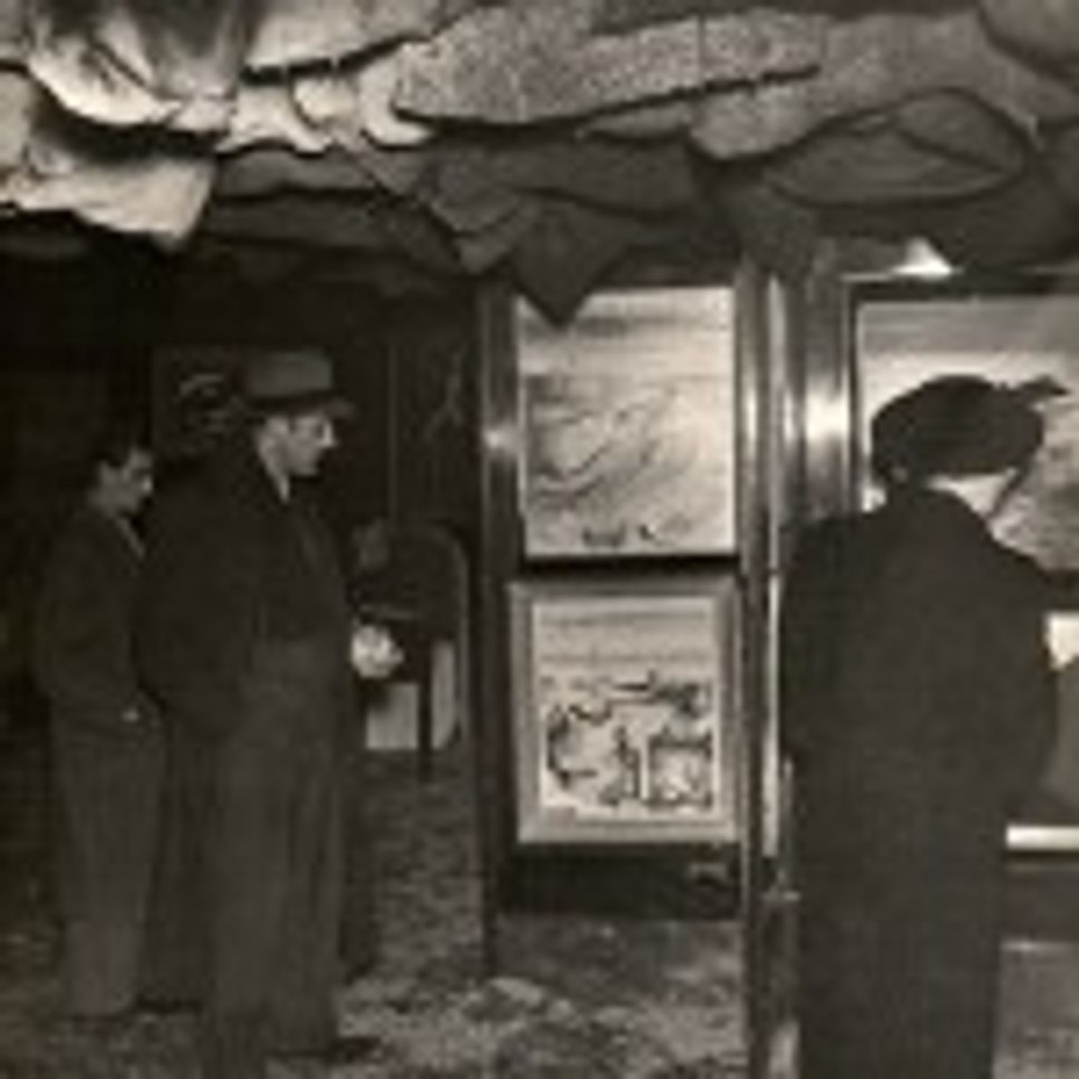 Vue de l’Exposition internationale du surréalisme, la salle principale. Des visiteurs admirent des œuvres placées sur des portes « revolver ».