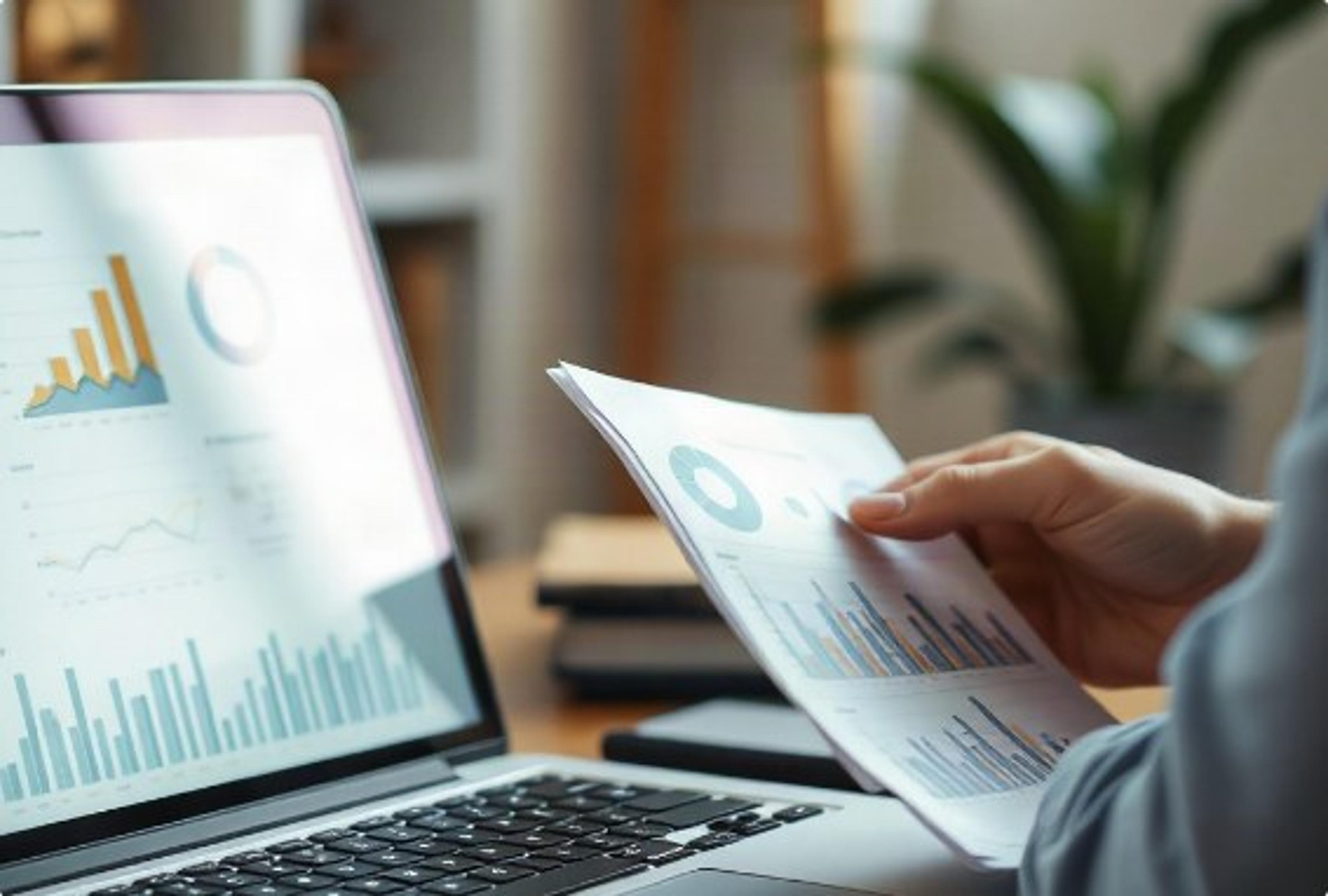 Analyst reviewing printed financial charts beside a laptop