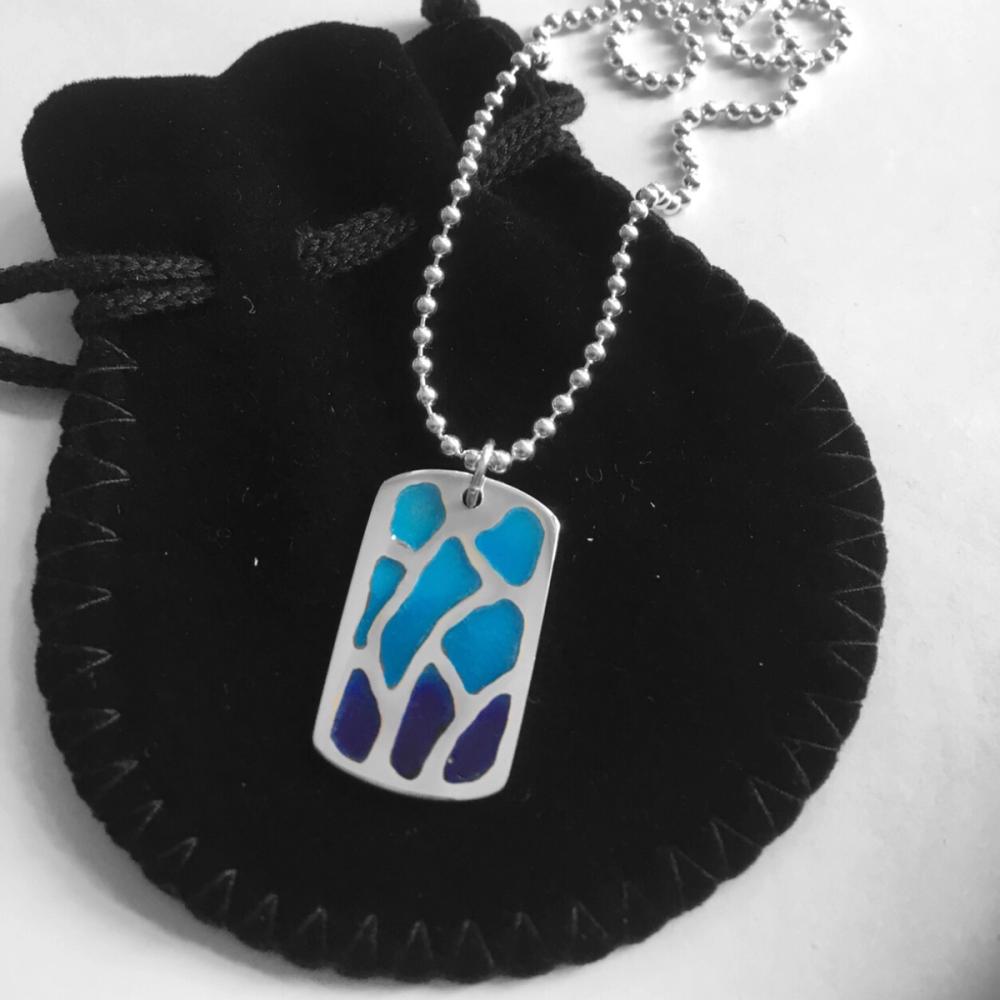 Final polished dog tag pendant made of silver, with a dark to light blue gradient sat on a black pouch