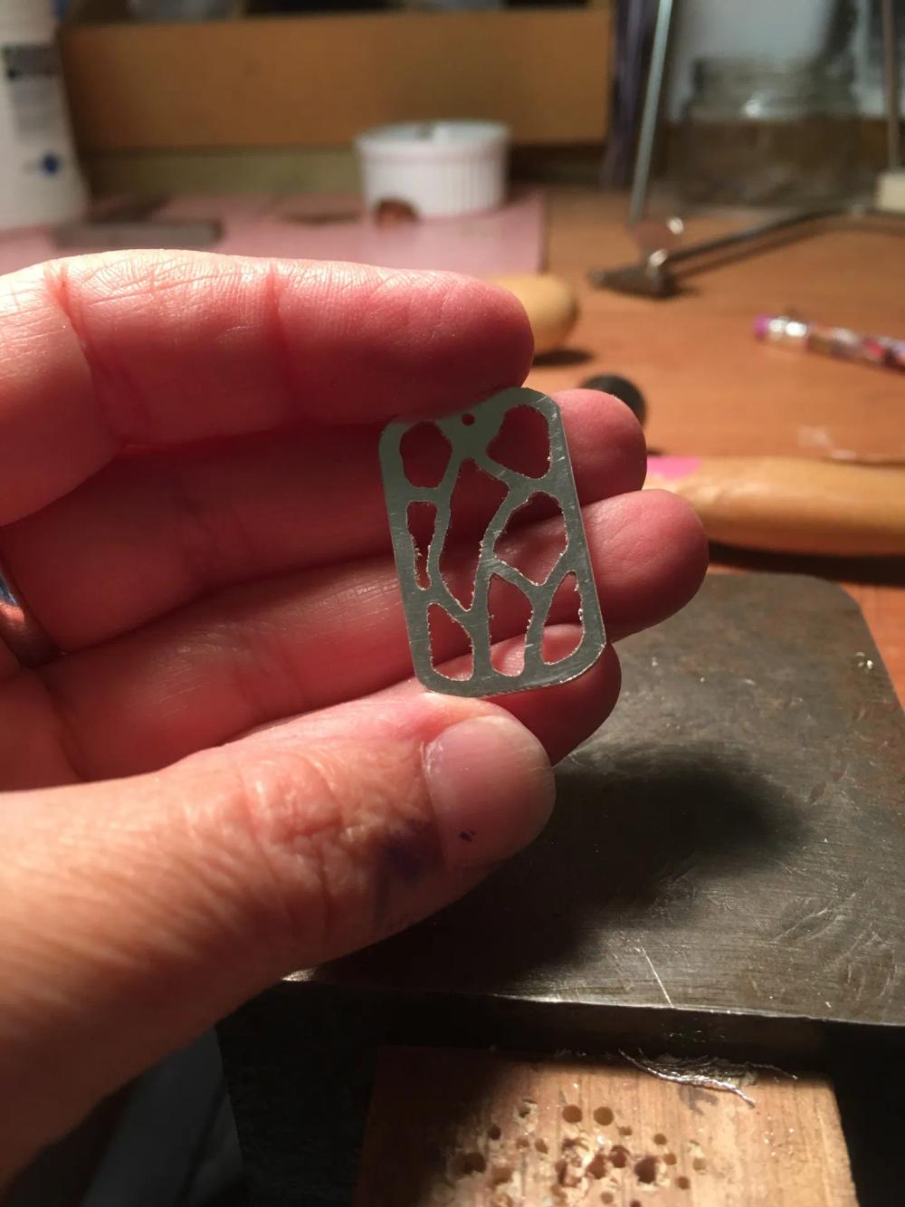 Fluid shapes cut out of silver dog tag pendant