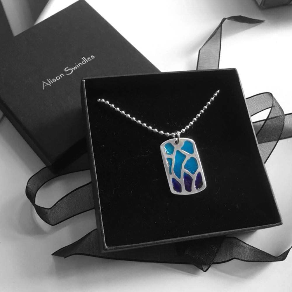 Silver dog tag pendant necklace with dark to light blue enamel gradient design in a black box