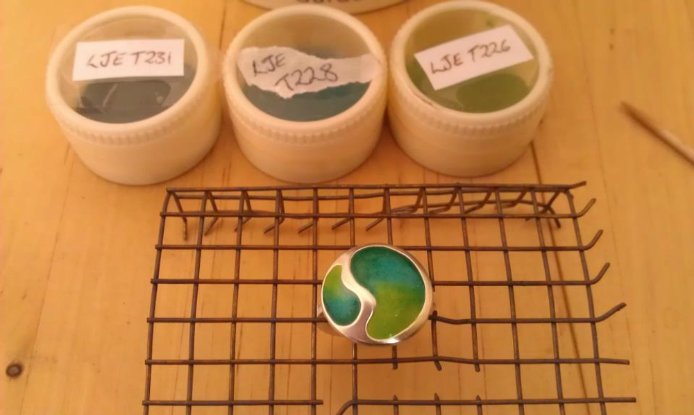 Silver ring with a green gradient enamel design sat on a wire cooling rack