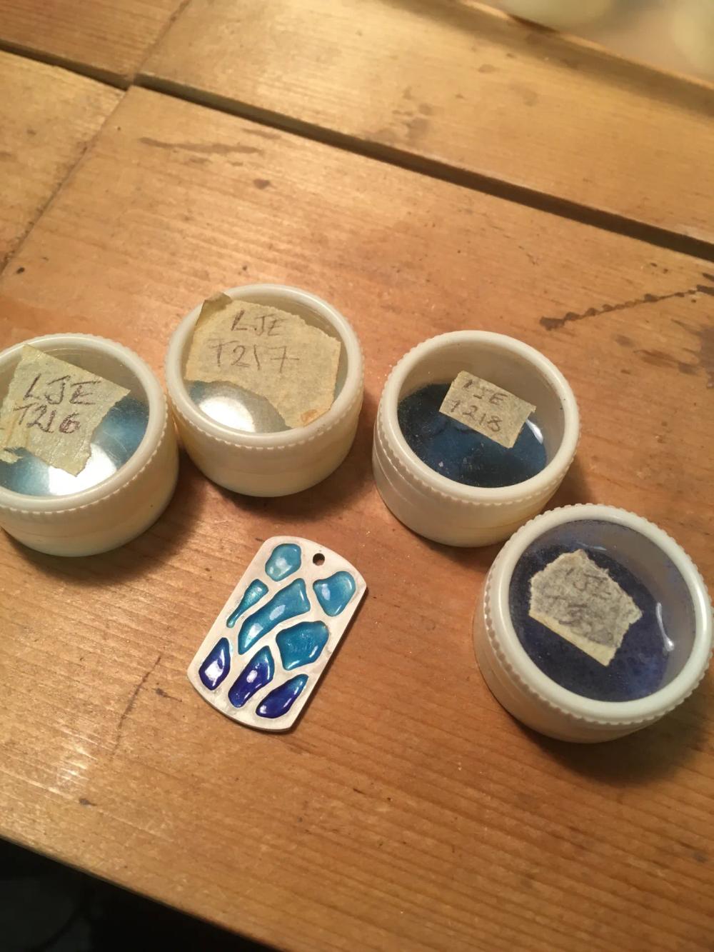 Fired pendant next to the pots of enamel powder used on it