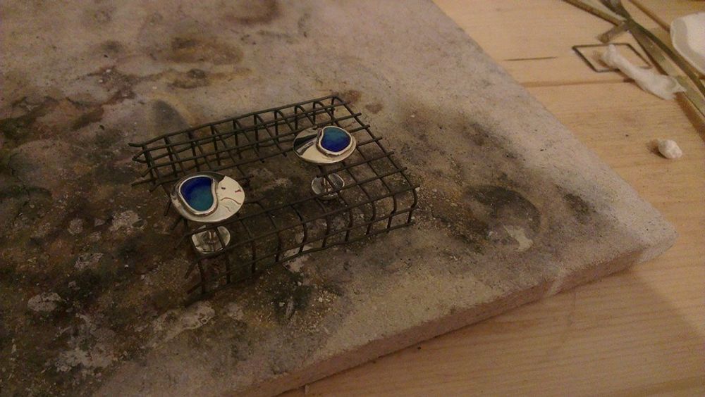 Silver cufflinks with blue enamel sat in wire cooling rack