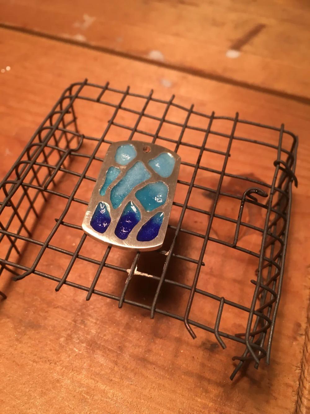Silver and enamel pendant on wire cooling rack after being fired three times