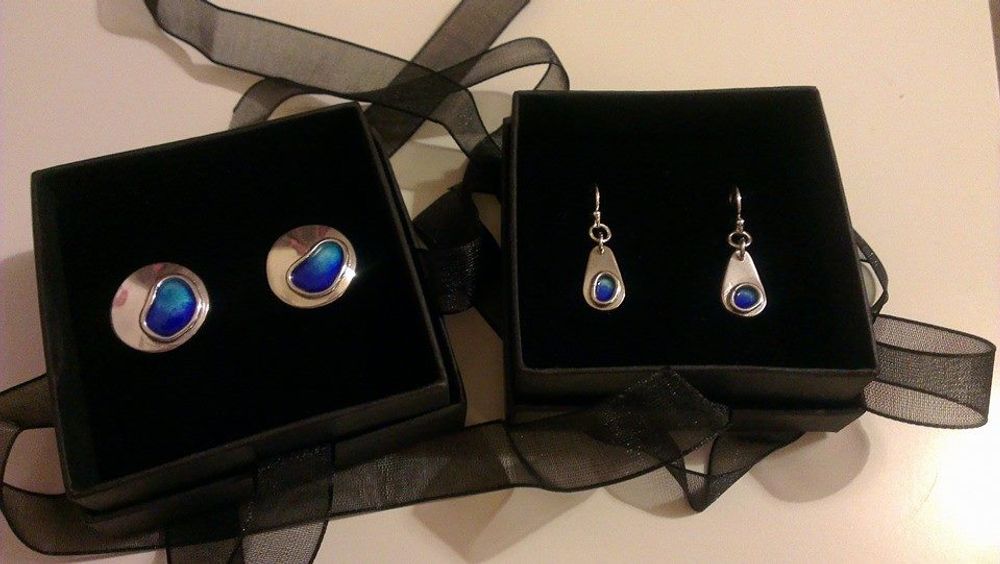 Silver with blue enamel cufflinks in black box next to another black box of silver and enamel earrings