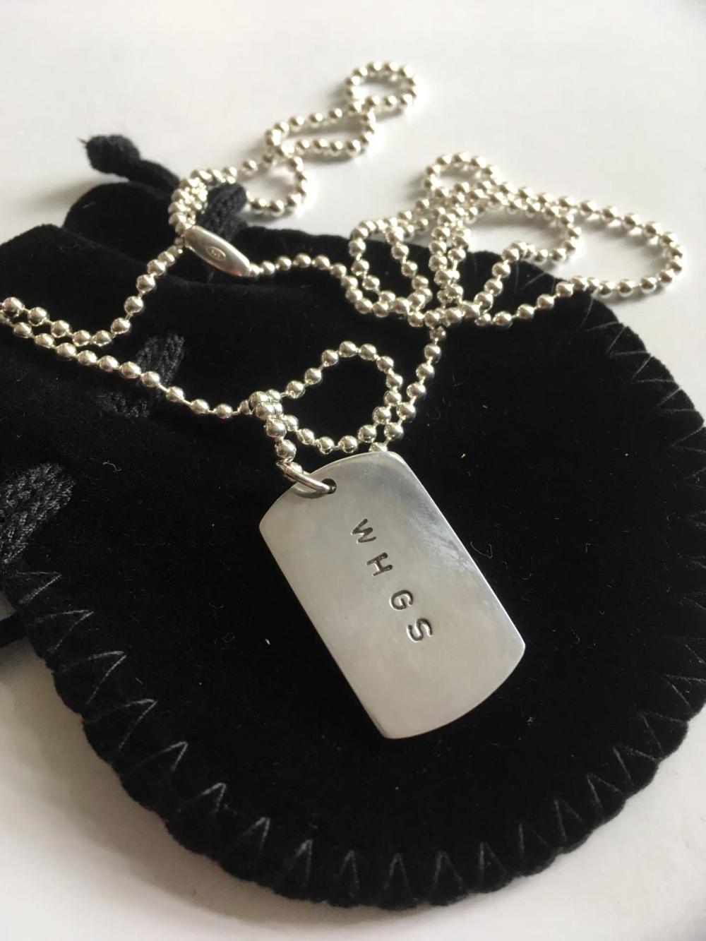 Reverse side of silver pendant necklace with the letters "W H G S" embossed on it