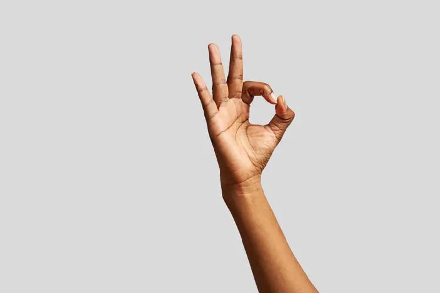 A hand making the 'OK' gesture - thumb and index finger forming a circle, other three fingers extended.