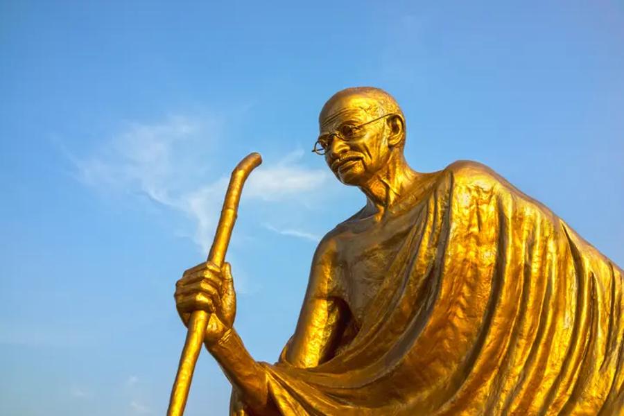 A large, gold statue of Gandhi with a clear blue sky in the background
