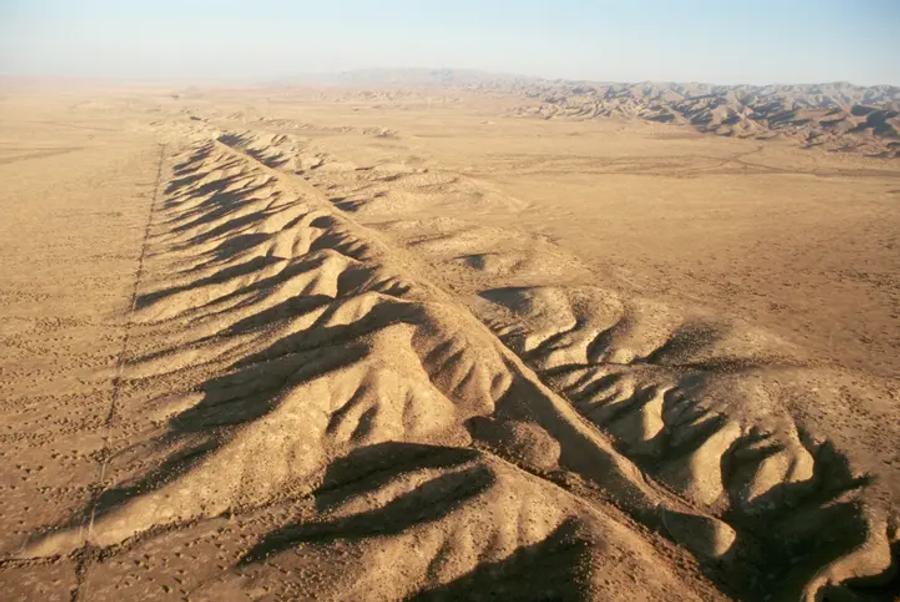 An aerial view of a long, narrow ridge running diagonally across dry, golden-brown hills and plains, the visible line of a geological fault.