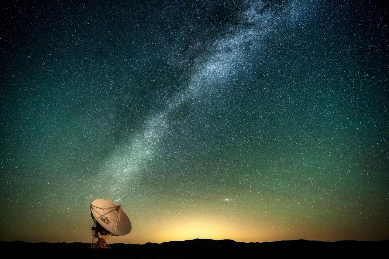 Radio telescope dish set against a backdrop of Milky Way galaxy