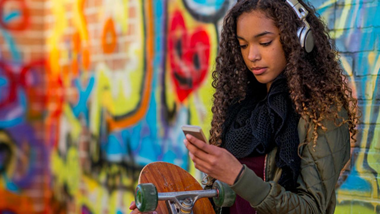 Girl on phone listening to music with graffiti wall behind her