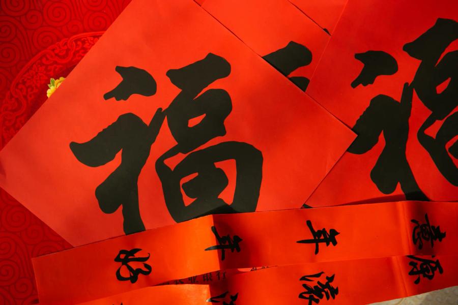 Overlapping sheets of red paper with bold black Chinese calligraphy, including the character 福 (fortune), arranged on a red patterned background.