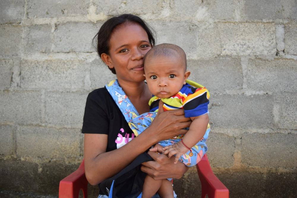 Maria sits with her baby outside the health post in Manuato. After attending nutrition counselling and cooking classes, she's seen her baby's health and weight improve. Photo: ChildFund Timor-Leste.