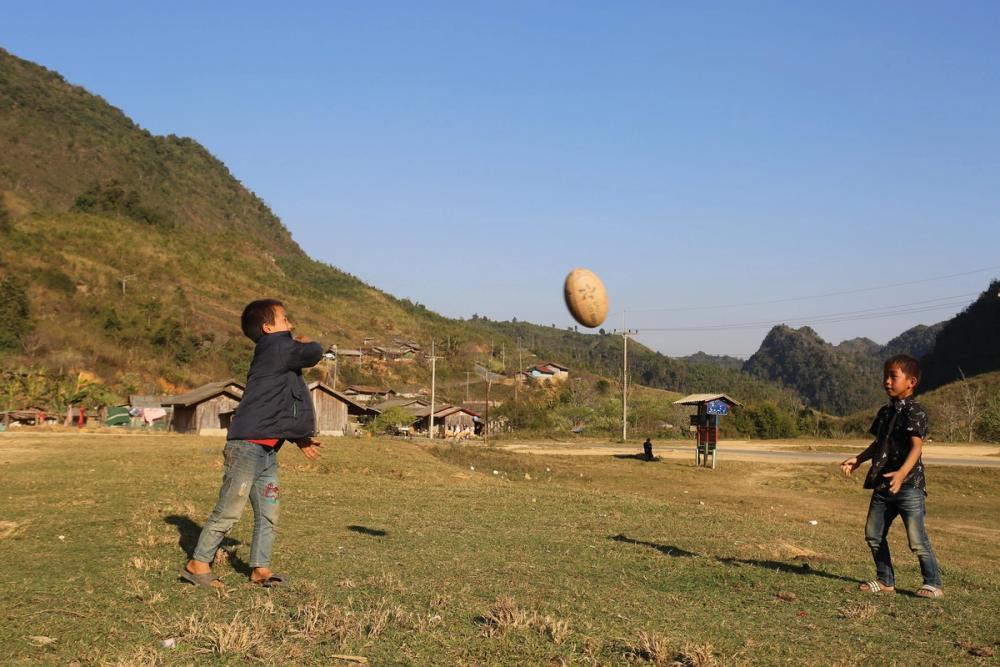 Two boys in a rural area throw a rugby ball to each other