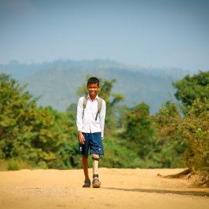 Seila walking to school with the aid of his leg brace.