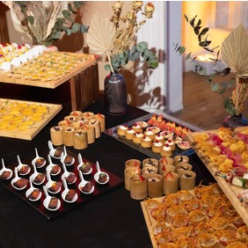 Un buffet traiteur garni de bouchées salées et sucrées disposées sur des plateaux en bois et en ardoise, décoré de fleurs séchées et d'eucalyptus.