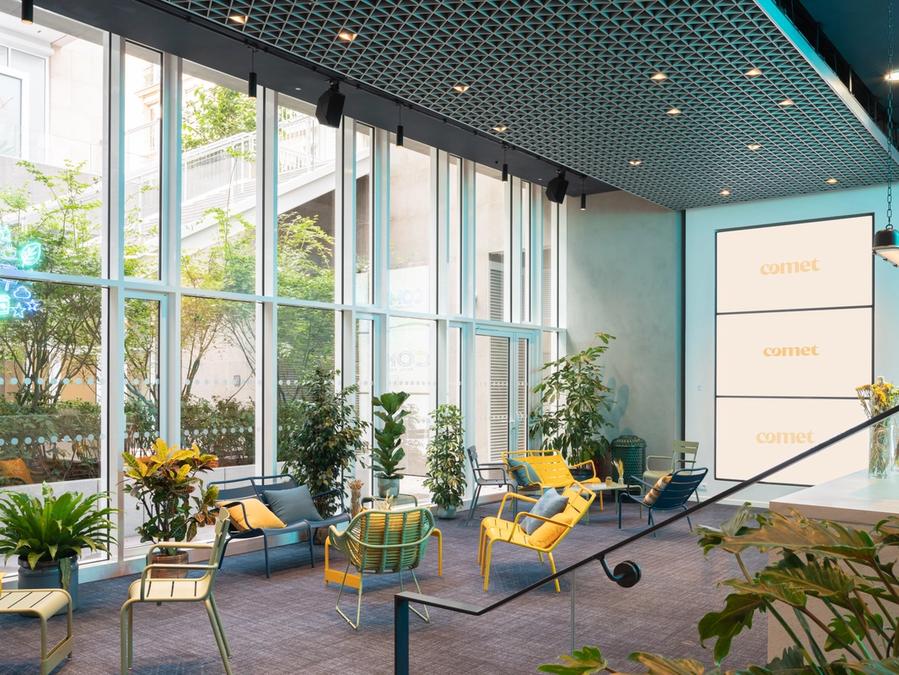 Des fauteuils jaunes et des plantes baignés de lumière derrière la verrière du jardin d'hiver de Comet Bourse