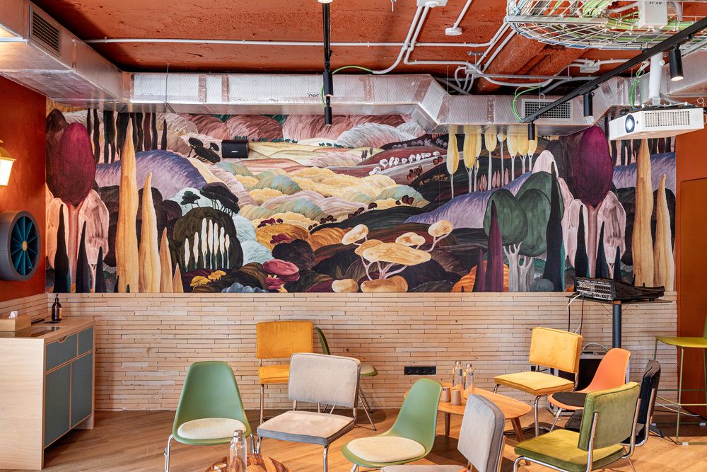 Un mural que representa un paisaje onírico de colinas, árboles y setas gigantes, sobre una zona de reunión.