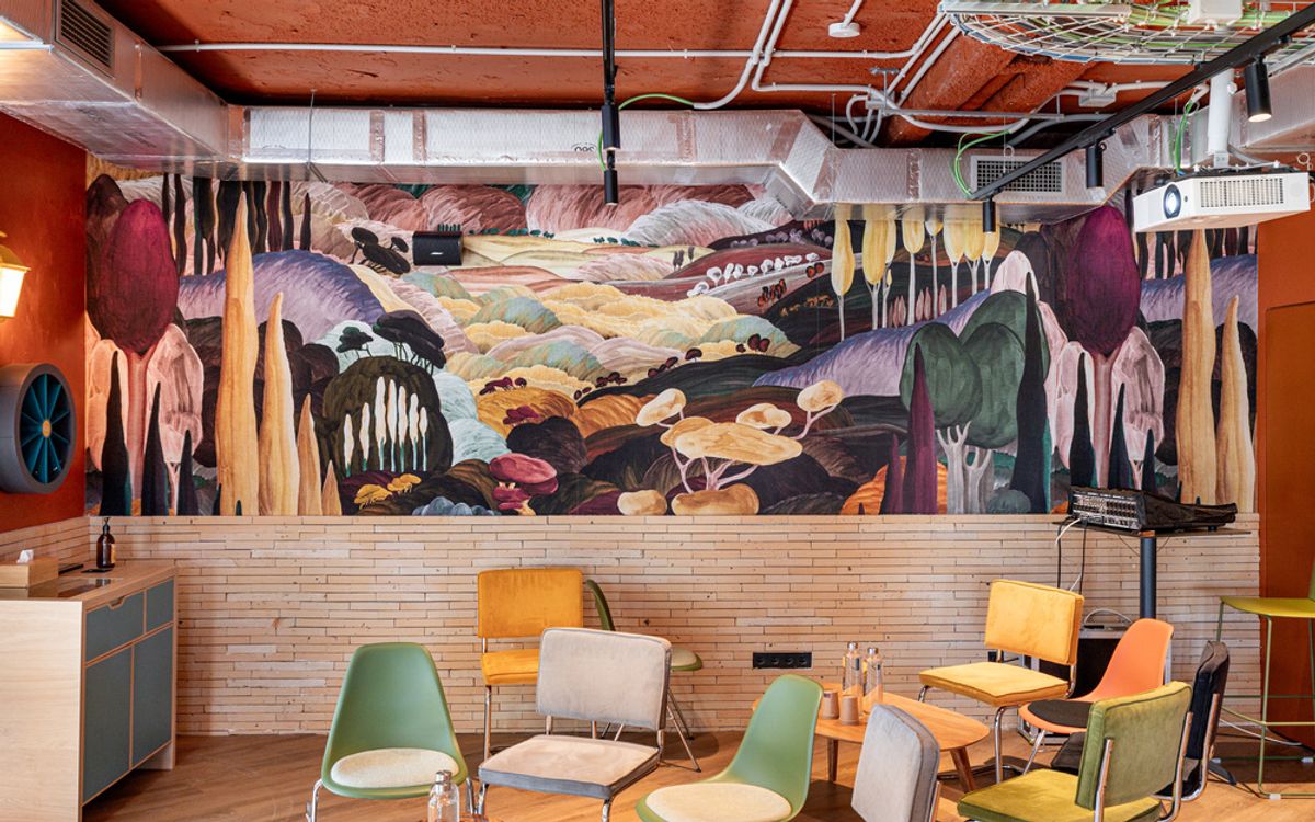 Un mural que representa un paisaje onírico de colinas, árboles y setas gigantes, sobre una zona de reunión.