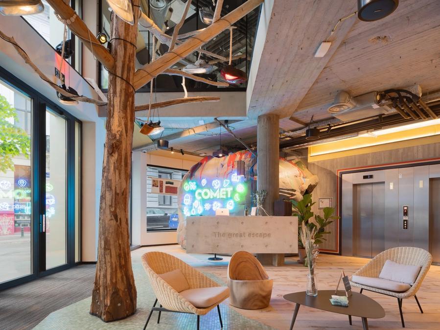 Le lobby de Comet Louise, son arbre central, ses fauteuils en rotin et l'enseigne néon au-dessus du comptoir