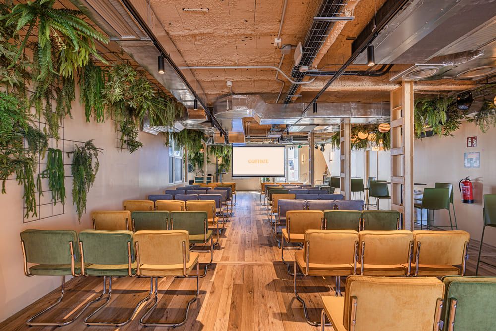 A room in theatre layout with yellow and green chairs, under hanging ferns, facing a screen showing the Comet logo.