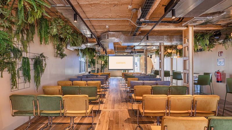 A room in theatre layout with yellow and green chairs, under hanging ferns, facing a screen showing the Comet logo.