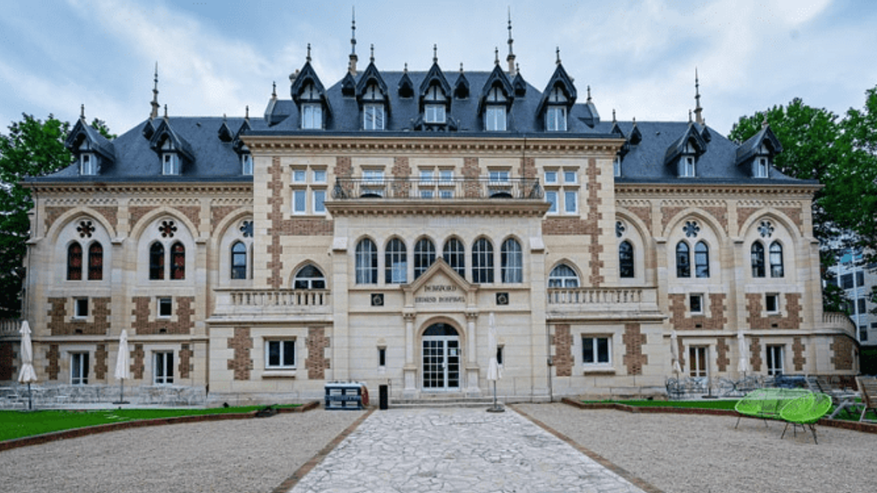 La fachada neogótica del castillo de Levallois, rematada por tejados de pizarra, al final de un camino de grava bordeado de césped.