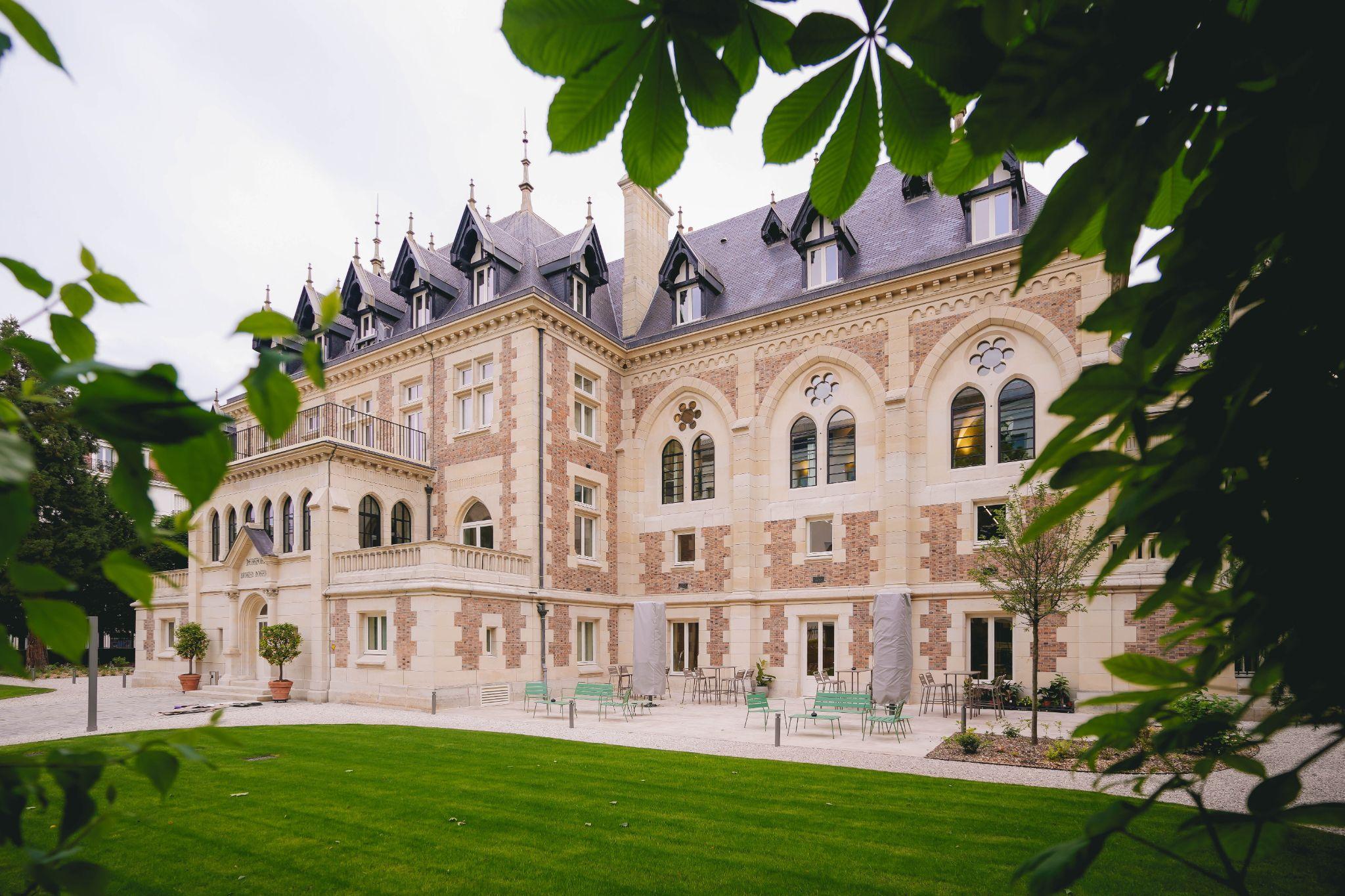The neo-Gothic façade of Le Grand Comet in Levallois-Perret, seen from the private garden through the foliage