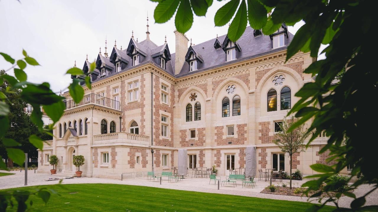The neo-Gothic façade of Le Grand Comet in Levallois-Perret, seen from the private garden through the foliage