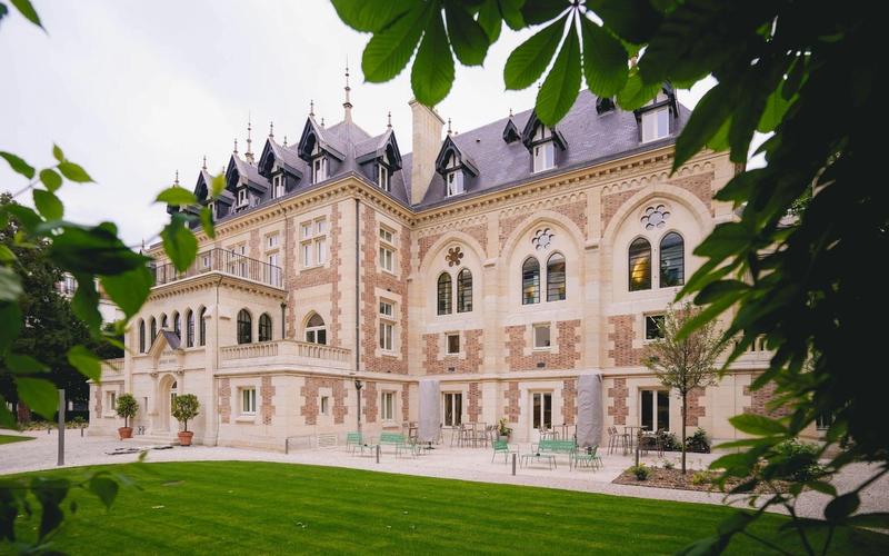 The neo-Gothic façade of Le Grand Comet in Levallois-Perret, seen from the private garden through the foliage