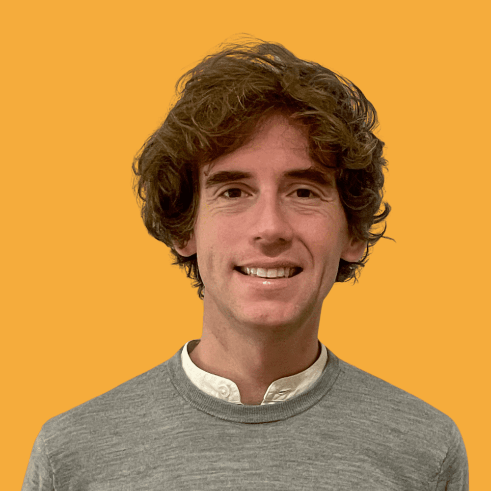 Frédéric Walter, met bruin krullend haar en een grijze trui over een wit hemd, tegen een gele achtergrond.