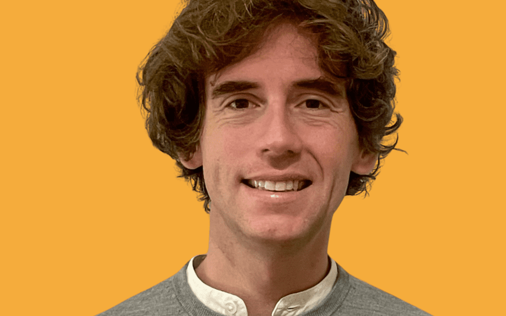 Frédéric Walter, cheveux bouclés bruns et pull gris sur chemise blanche, sur fond jaune.