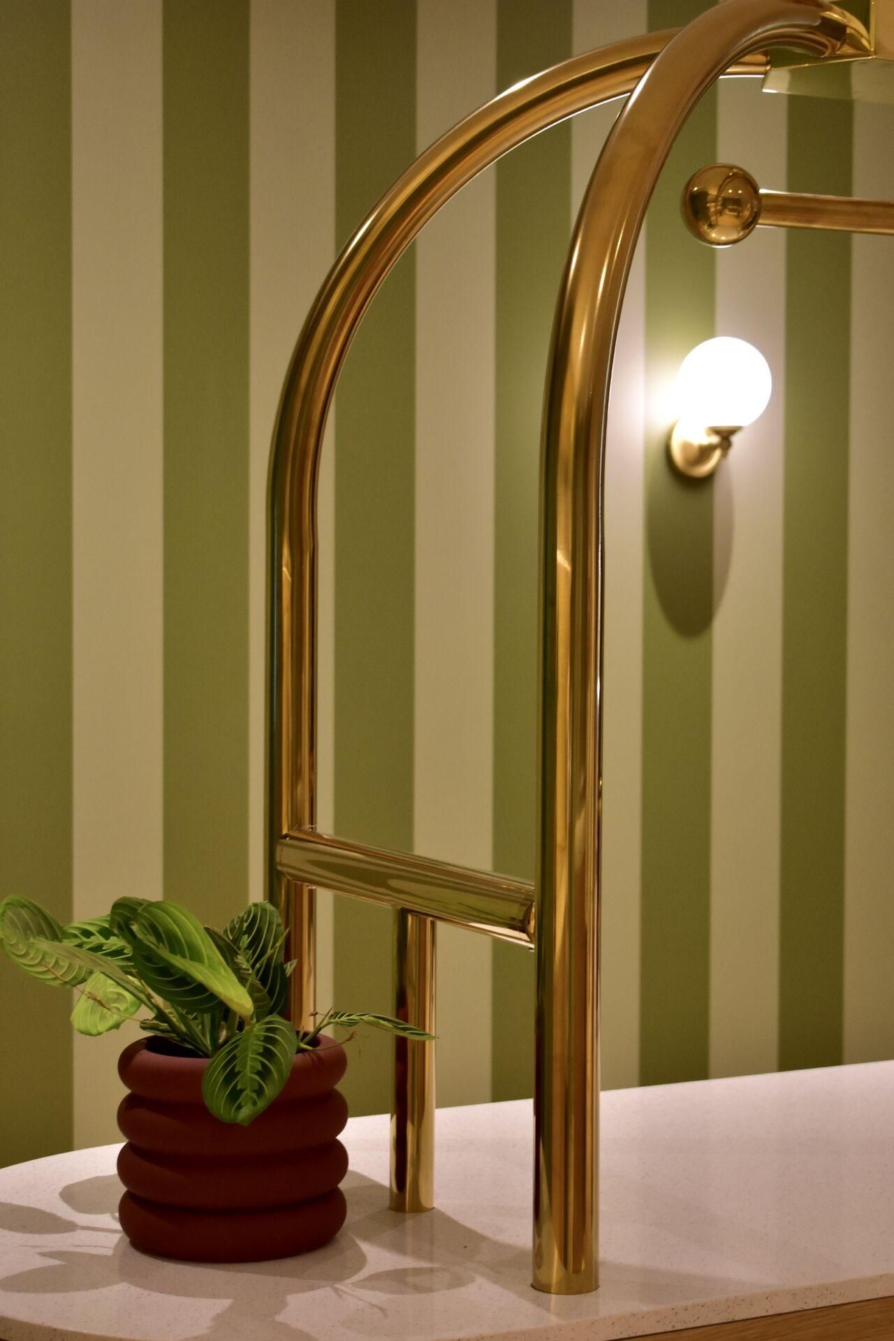 Detail of the interior set design: green striped wall and polished brass handrail