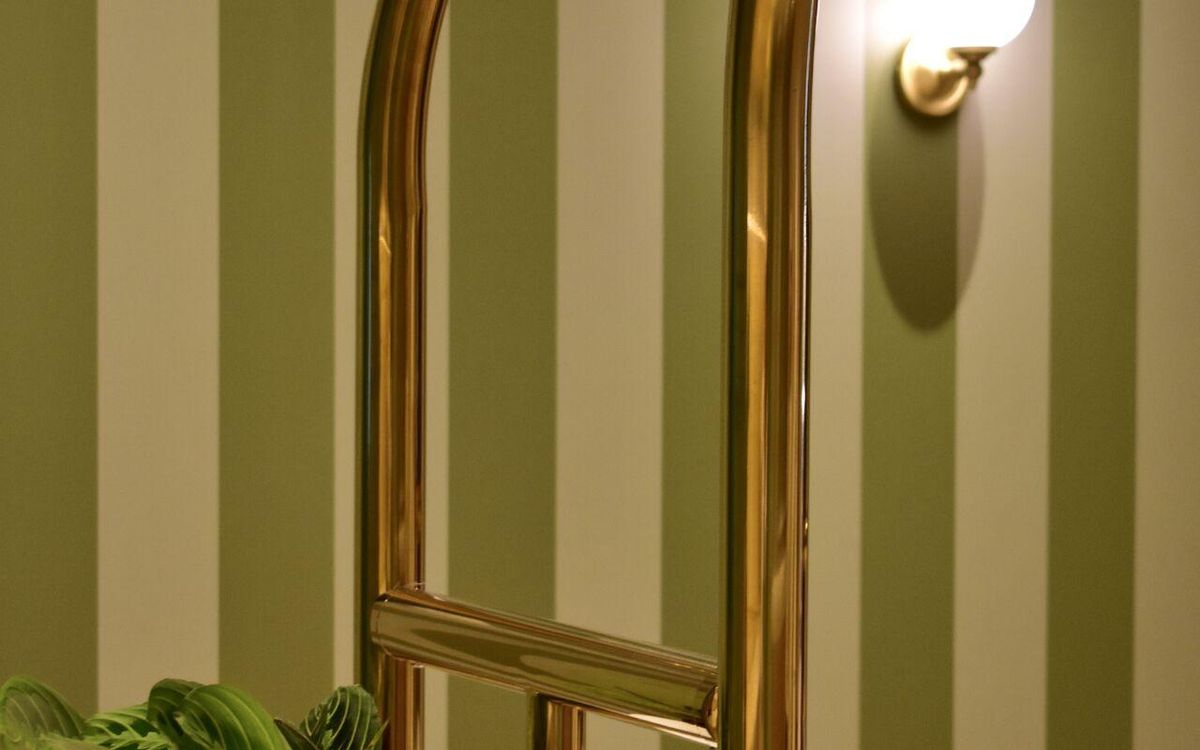 Detail of the interior set design: green striped wall and polished brass handrail