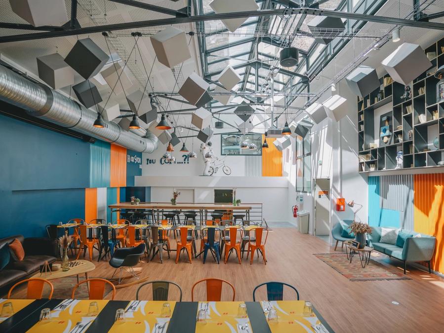 Vaste salle de Comet Ternes sous verrière, cubes suspendus et longues tablées entourées de chaises colorées
