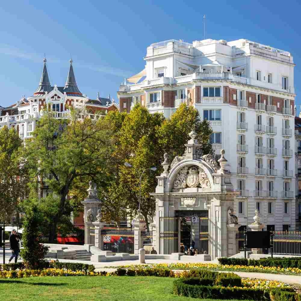 La monumental puerta de piedra del parque de El Retiro en Madrid y, tras los árboles, el edificio blanco que alberga Comet Retiro.