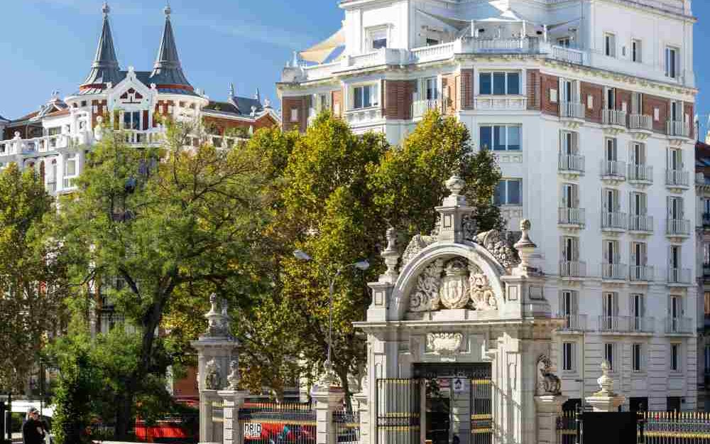 La porte monumentale en pierre du parc du Retiro à Madrid et, derrière les arbres, l'immeuble blanc qui abrite Comet Retiro.
