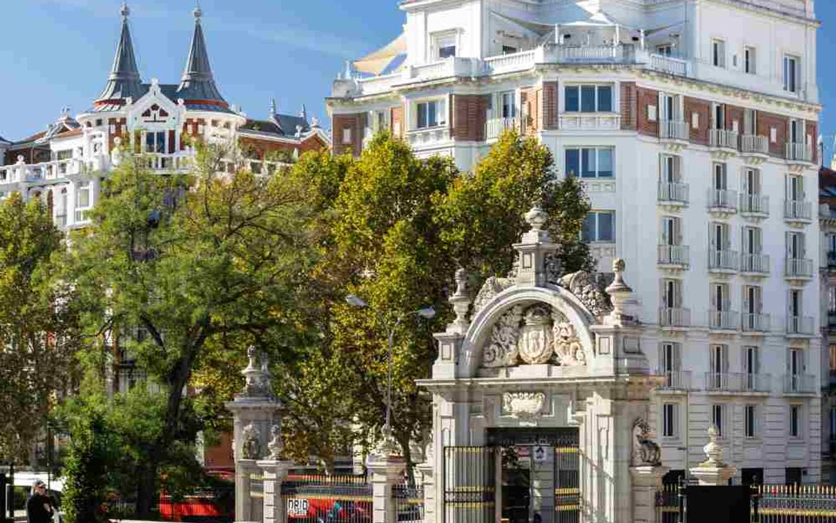 The monumental stone gateway to Retiro Park in Madrid and, behind the trees, the white building that houses Comet Retiro.