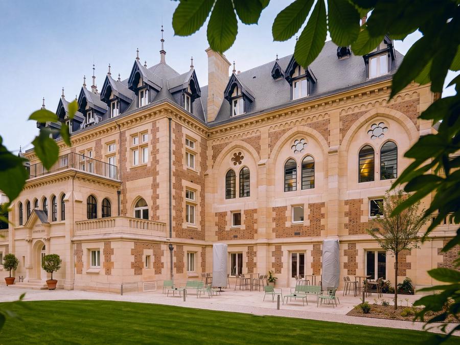 L'hôtel particulier de Comet Levallois et sa terrasse aux chaises vertes, vus depuis la pelouse du jardin