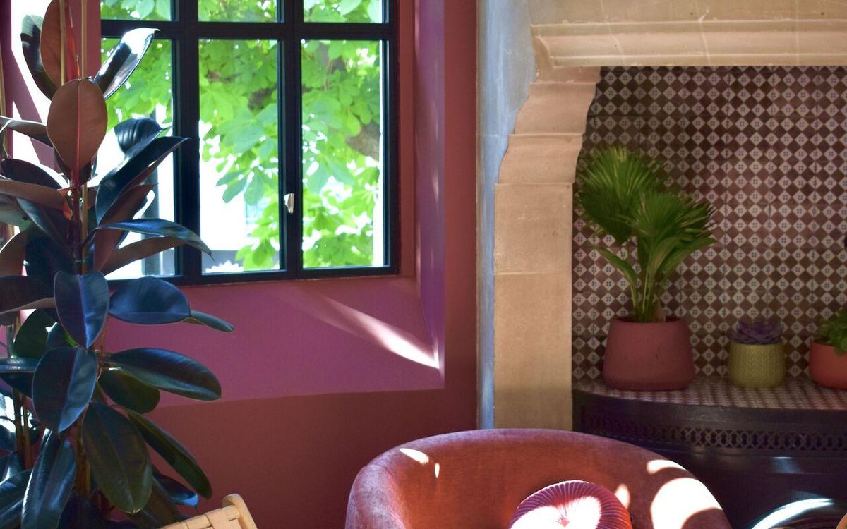 Lounge at Le Grand Comet with a stone fireplace, cognac leather armchair and a tall window onto the grounds