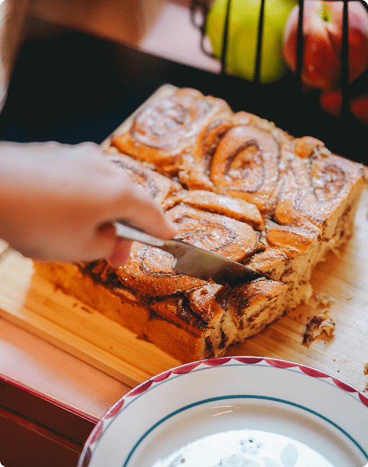 Une scène gourmande et spontanée autour d’un dessert généreux, découpé juste avant d’être partagé. La lumière douce, les textures dorées et la mise en scène naturelle évoquent une cuisine conviviale, sincère et réconfortante, pensée pour accompagner les moments d’échange.