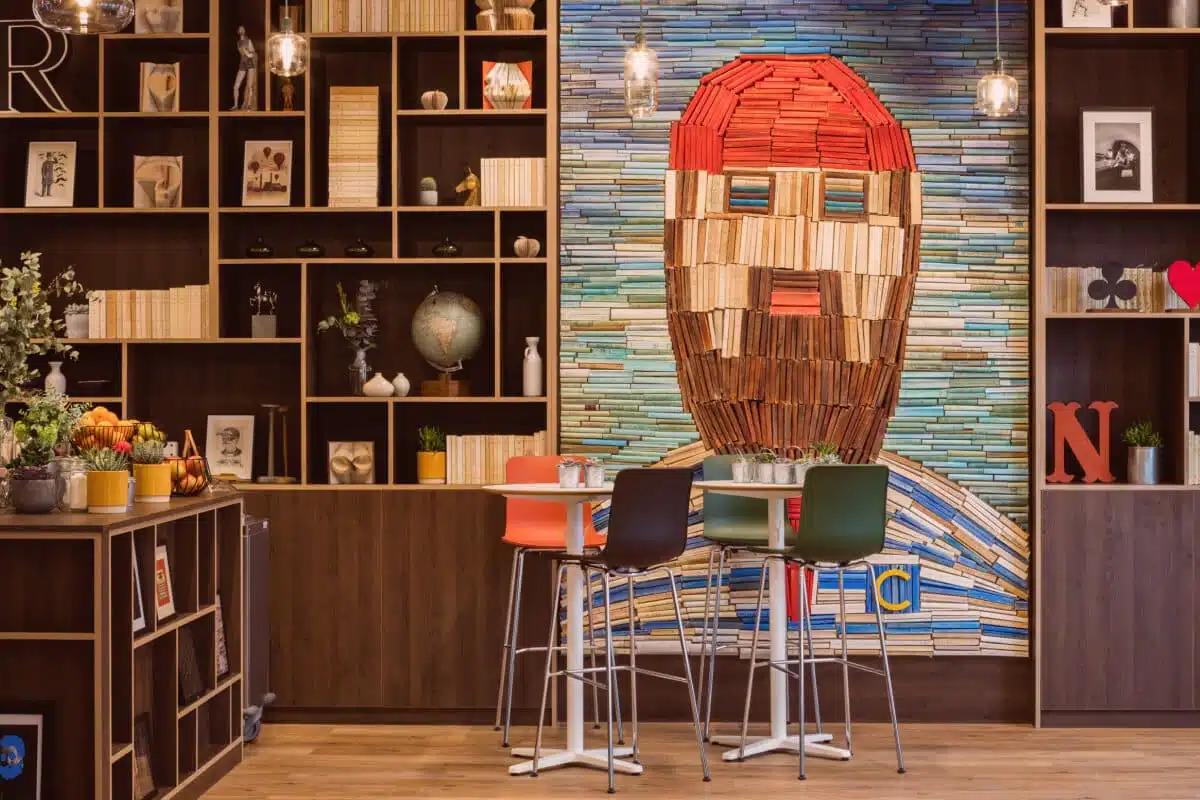Een warme en creatieve ruimte bij Comet Étoile, gekenmerkt door een bijzondere inrichting, een wandbibliotheek en een artistieke muurschildering gemaakt van boeken. Het beeld benadrukt een inspirerende seminarlocatie, waar design, gezelligheid en een huiselijke sfeer samenkomen om teams een omgeving te bieden die tegelijk professioneel, origineel en onvergetelijk is.