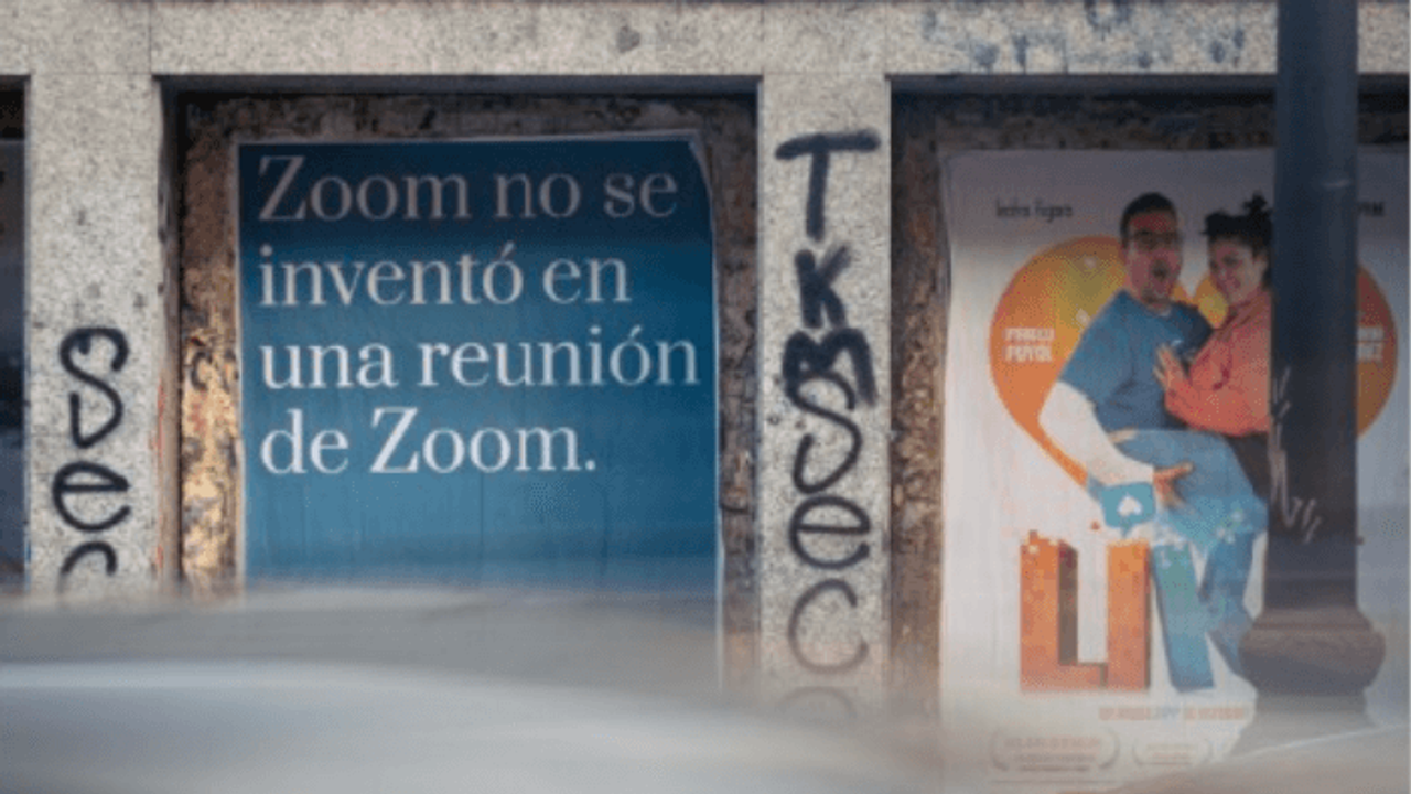 A blue poster pasted on a Madrid shopfront reading « Zoom no se inventó en una reunión de Zoom ».