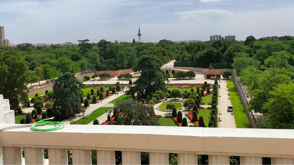 Uitzicht vanaf een terras met balustrade over de gesnoeide tuinen van het Retiro-park en, verderop, de daken van Madrid.