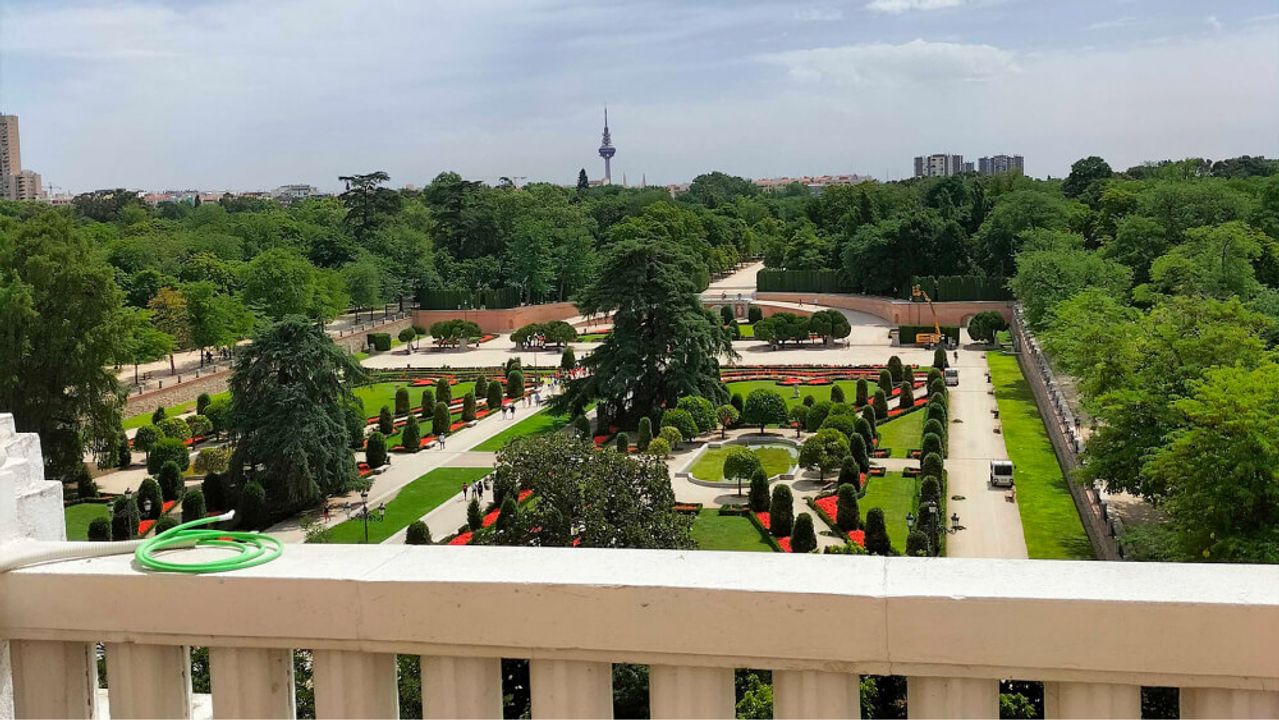 Uitzicht vanaf een terras met balustrade over de gesnoeide tuinen van het Retiro-park en, verderop, de daken van Madrid.
